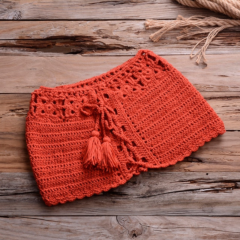 Crochet bikini set in vibrant orange color, with textured patterns and tassel details, displayed on a rustic wooden background with natural wheat stalks.