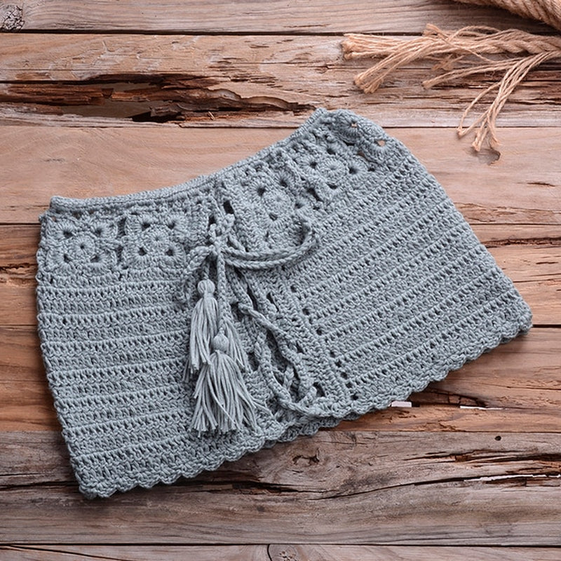 Cozy crocheted gray shorts with tasseled drawstring on rustic wooden background, stylish summer beachwear.