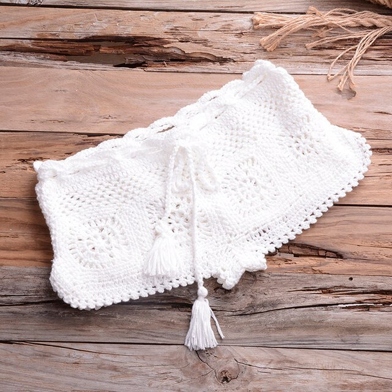 Crocheted white bikini set on rustic wooden background, stylish summer beachwear with tassel details, cozy knitted swimsuit for beach season.